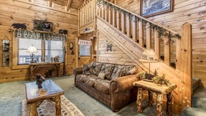 Ein gemütliches Blockhaus-Interieur mit einer Holztreppe, einem Ledersofa und einem rustikalen Esstisch.