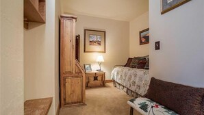 Un dormitorio con cama, armario de madera, mesita de noche con lámpara y un cuadro en la pared.