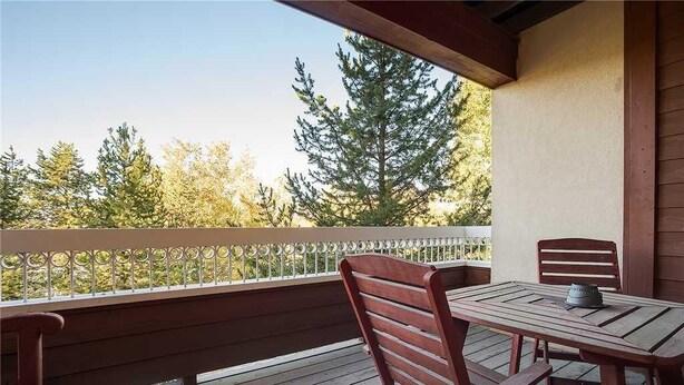 Una terraza de madera con una mesa y sillas, con vista a un área boscosa.