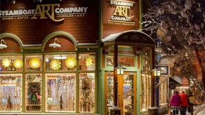 Tienda Steamboat Art Company con ventanas iluminadas y una calle nevada.