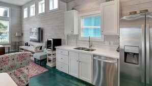 A modern kitchen with white cabinets, stainless steel appliances, and a window with blinds.