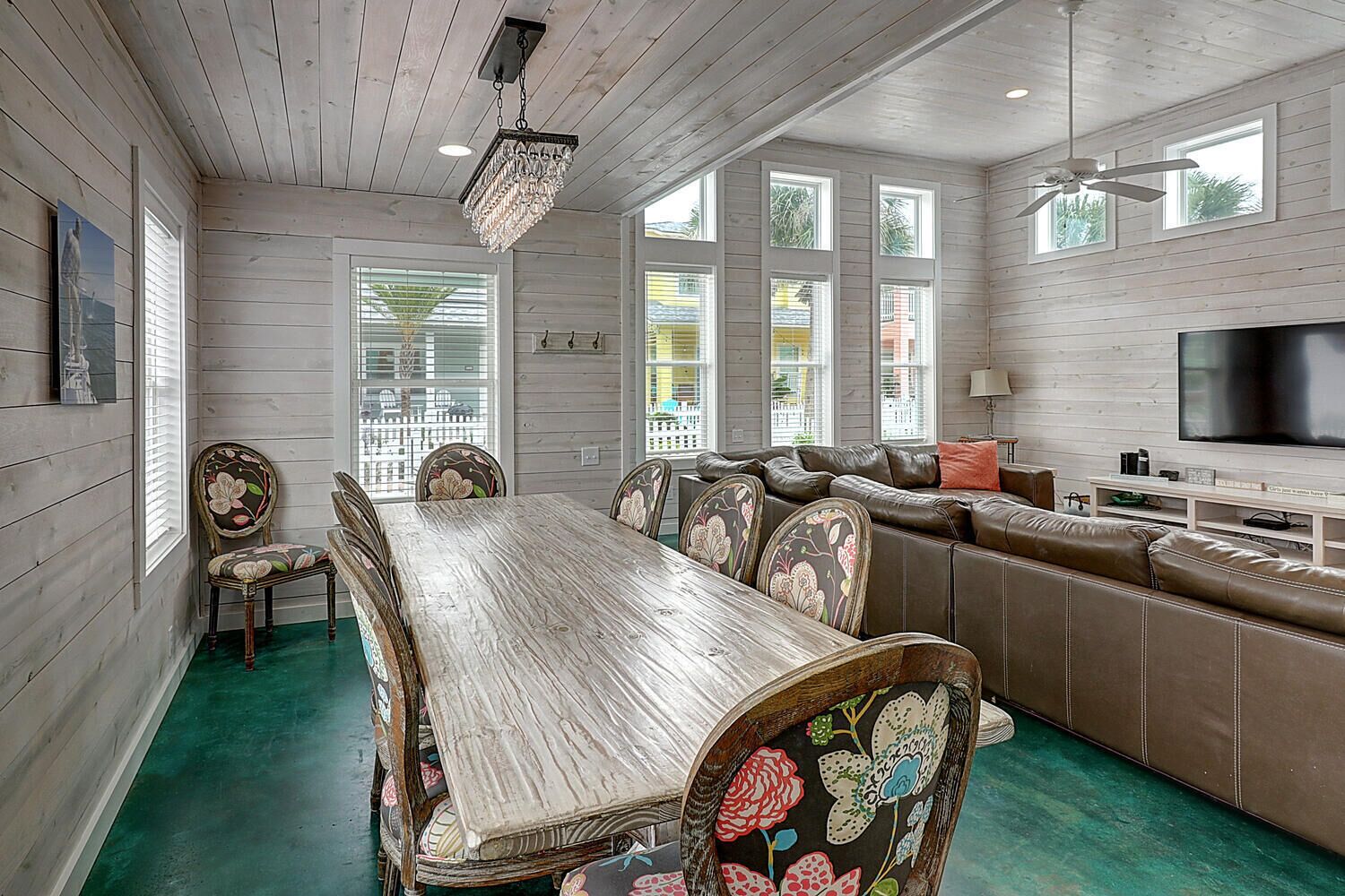 Une pièce spacieuse avec une longue table à manger en bois, des chaises à motifs floraux, un canapé en cuir et un grand téléviseur à écran plat.