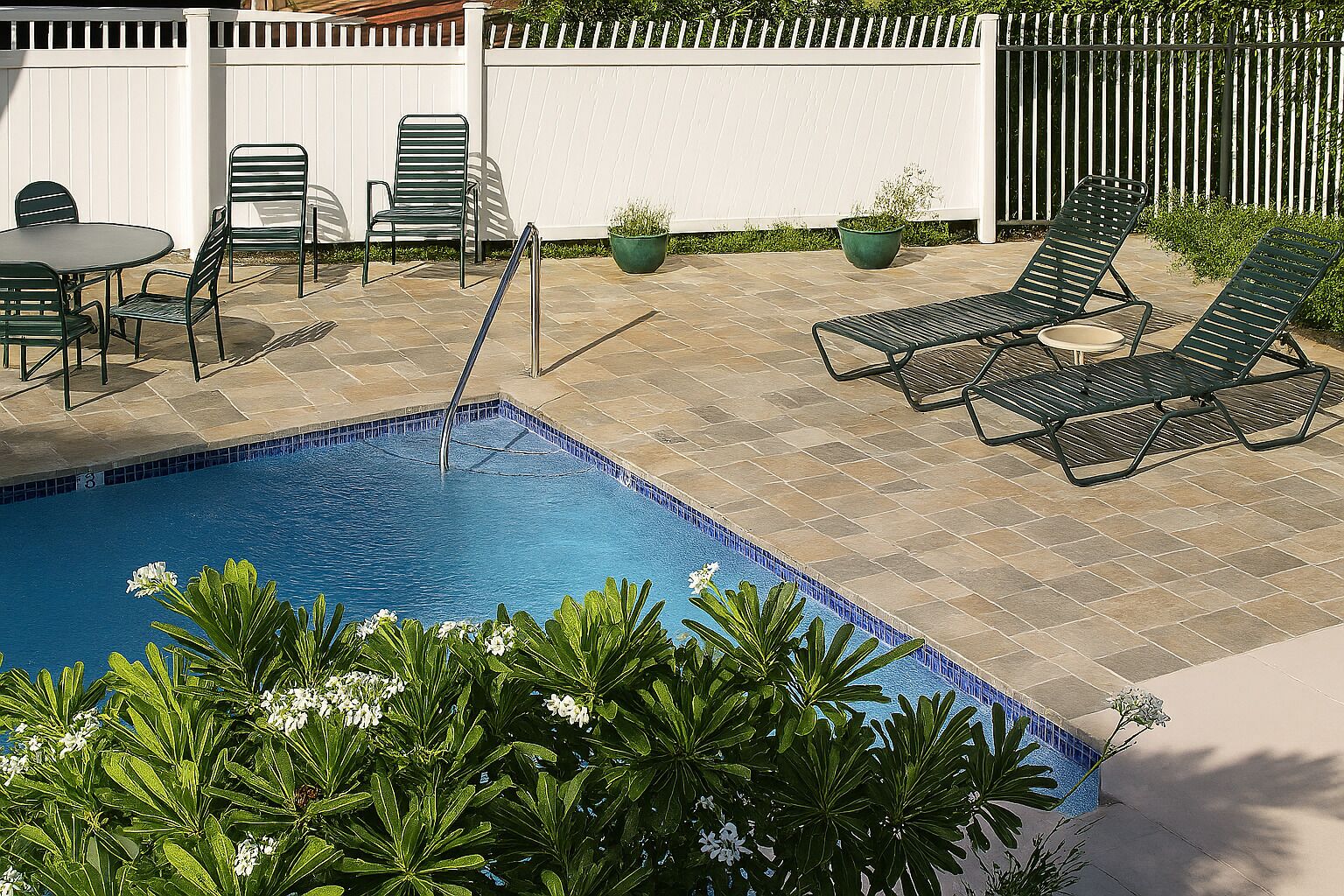 A swimming pool with a tiled deck, surrounded by lounge chairs and a table.