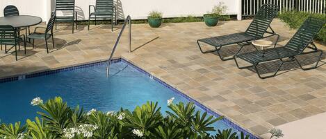 A swimming pool with a tiled deck, surrounded by lounge chairs and a table.