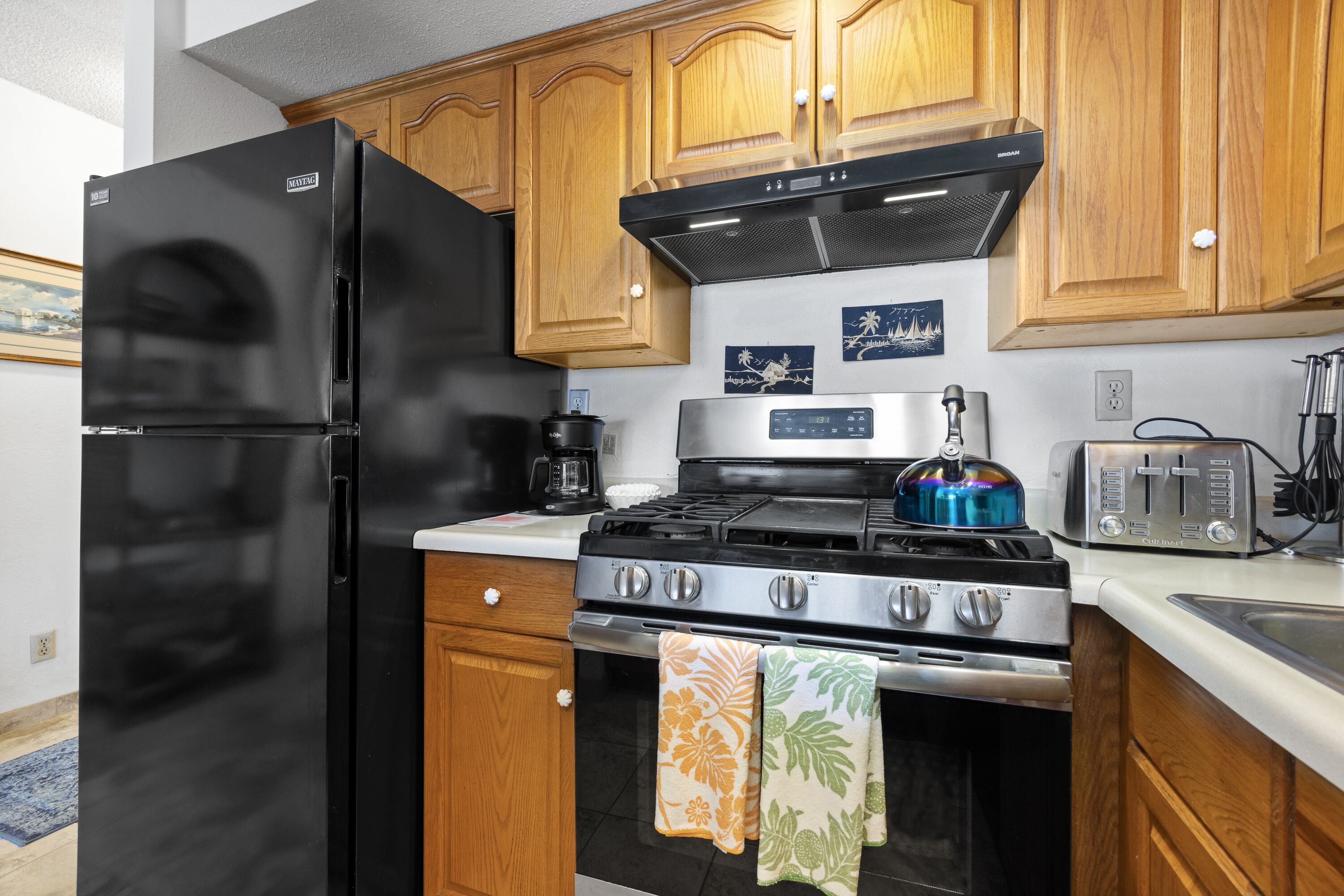 A kitchen with wooden cabinets, a black refrigerator, a stainless steel stove, and a toaster.