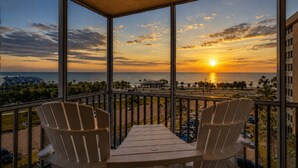 Un balcon avec deux chaises et une table, d’où l’on peut admirer le coucher de soleil sur l’océan.