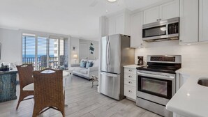 Une cuisine moderne équipée d’appareils électroménagers en acier inoxydable, un coin repas avec des chaises en osier et un balcon offrant une vue agréable.