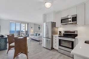 Une cuisine moderne équipée d’appareils électroménagers en acier inoxydable, un coin repas avec des chaises en osier et un balcon offrant une vue agréable.