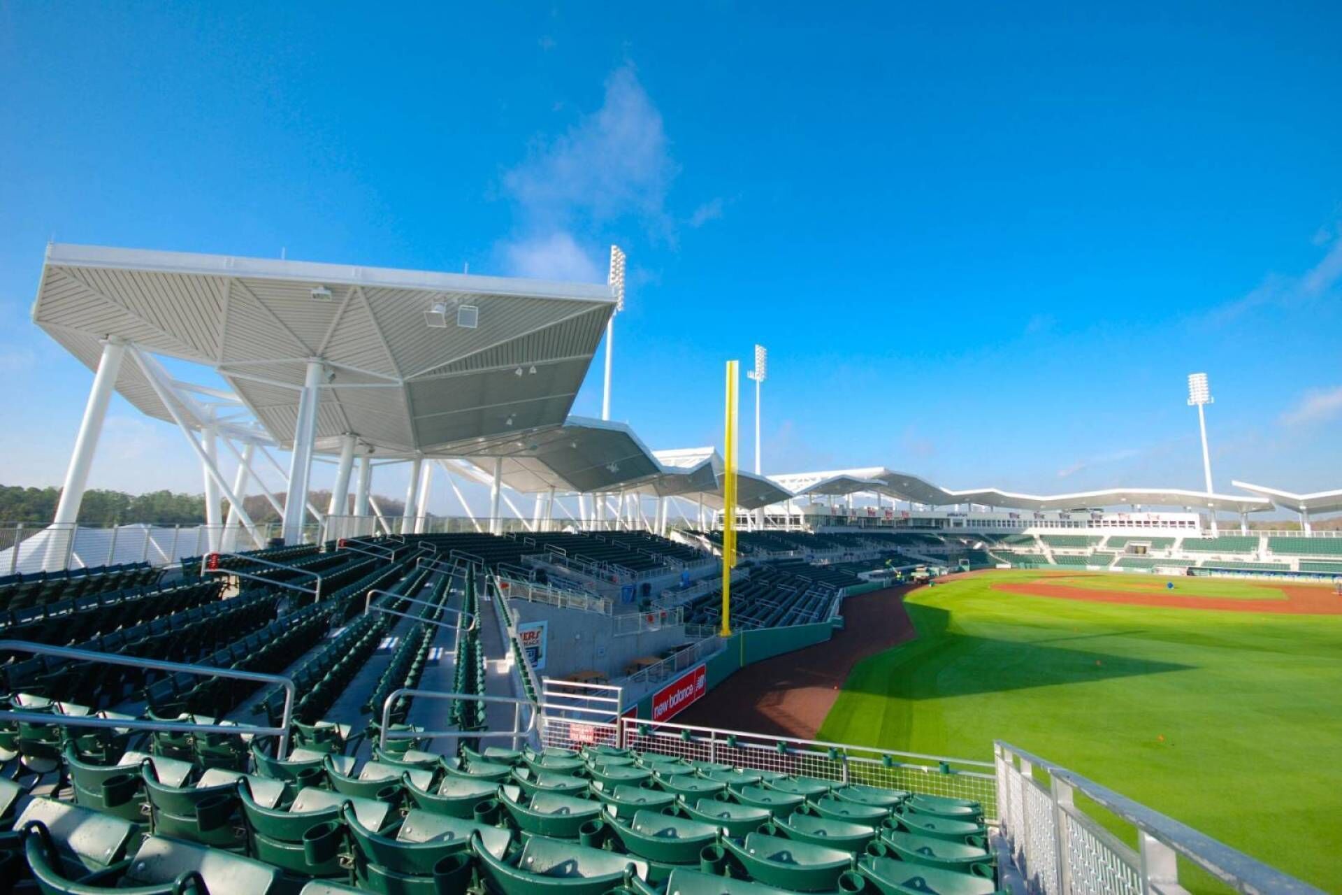 A stadium with multiple seating sections, a green field, and a clear blue sky.