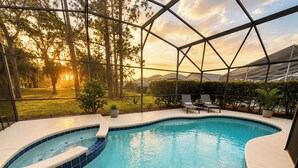Una piscina con un jacuzzi, rodeada de sillas de descanso y plantas en macetas, con vistas a árboles y montañas.