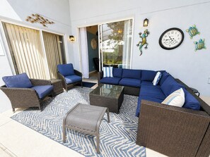 A sunlit patio with wicker furniture, a glass coffee table, and a wall clock. - Comfortable & Spacious Pool Home With Spa in Highlands Reserve - Golf Course View (Davenport)
