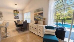 Una sala de estar moderna con comedor, un amplio ventanal con vistas a una piscina y una lámpara en el techo.