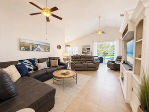 A spacious living room with a leather sofa, a recliner, a coffee table, and ceiling fans. - Comfortable & Spacious Pool Home With Spa in Highlands Reserve - Golf Course View (Davenport)