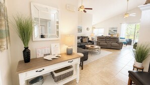 Amplia sala de estar con chimenea, comedor con mesa consola blanca y zona de estar con sofás y una mesa de centro.