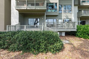 Un immeuble résidentiel à plusieurs étages, doté de balcons, d’un espace extérieur aménagé et couvert, et d’une haie bien entretenue.