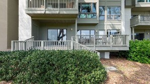 A multi-story residential building with balconies, a covered outdoor seating area, and a well-maintained hedge.