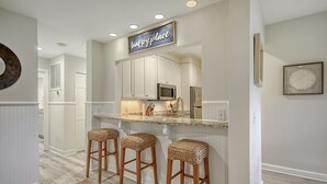 A kitchen with white cabinetry, a stainless steel refrigerator, a microwave, and a bar stool area.