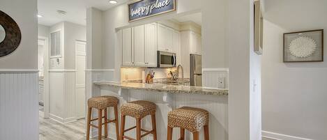 A kitchen with white cabinetry, a stainless steel refrigerator, a microwave, and a bar stool area.