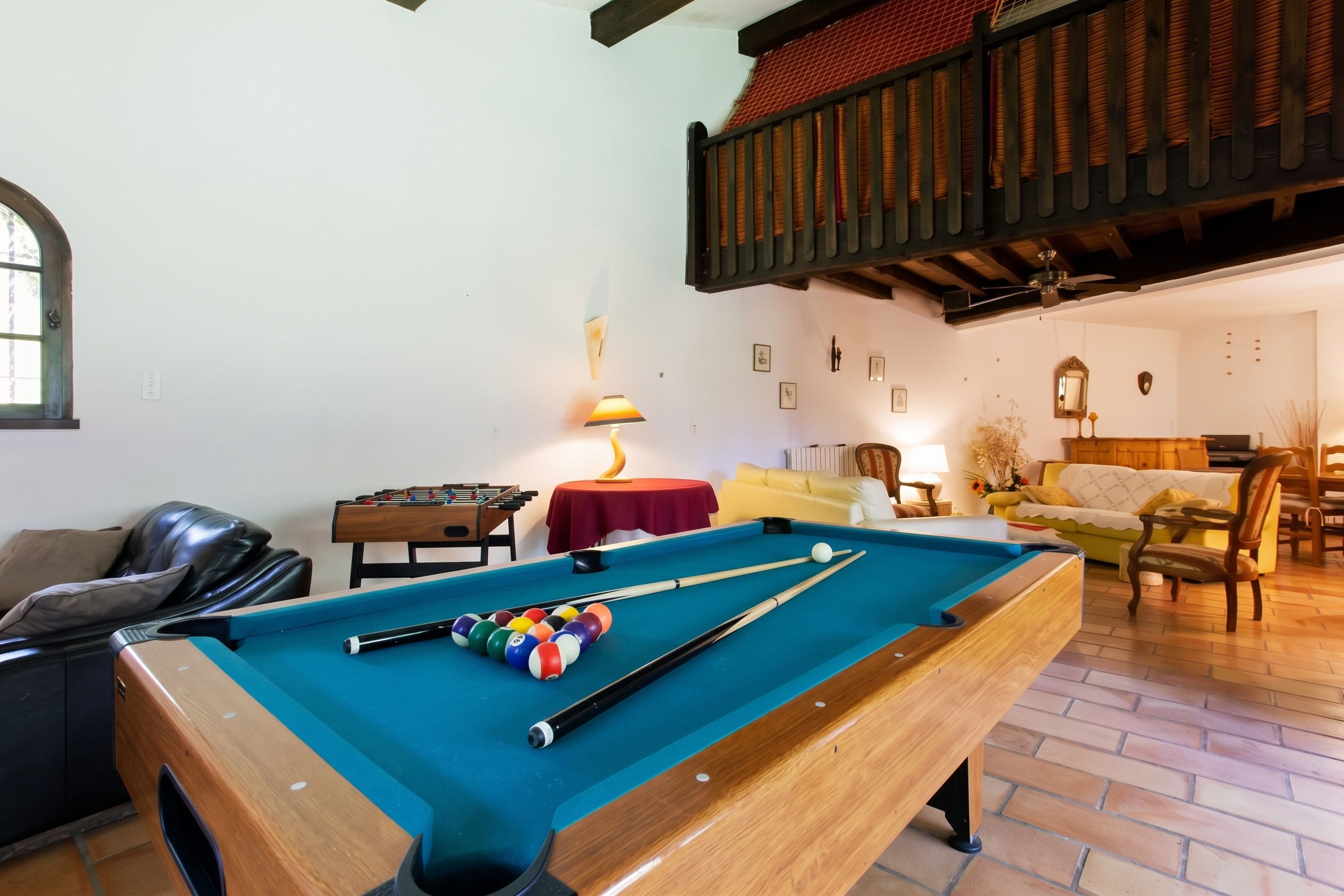 Een pooltafel in een kamer met een bank, een tafel met een lamp en een raam.