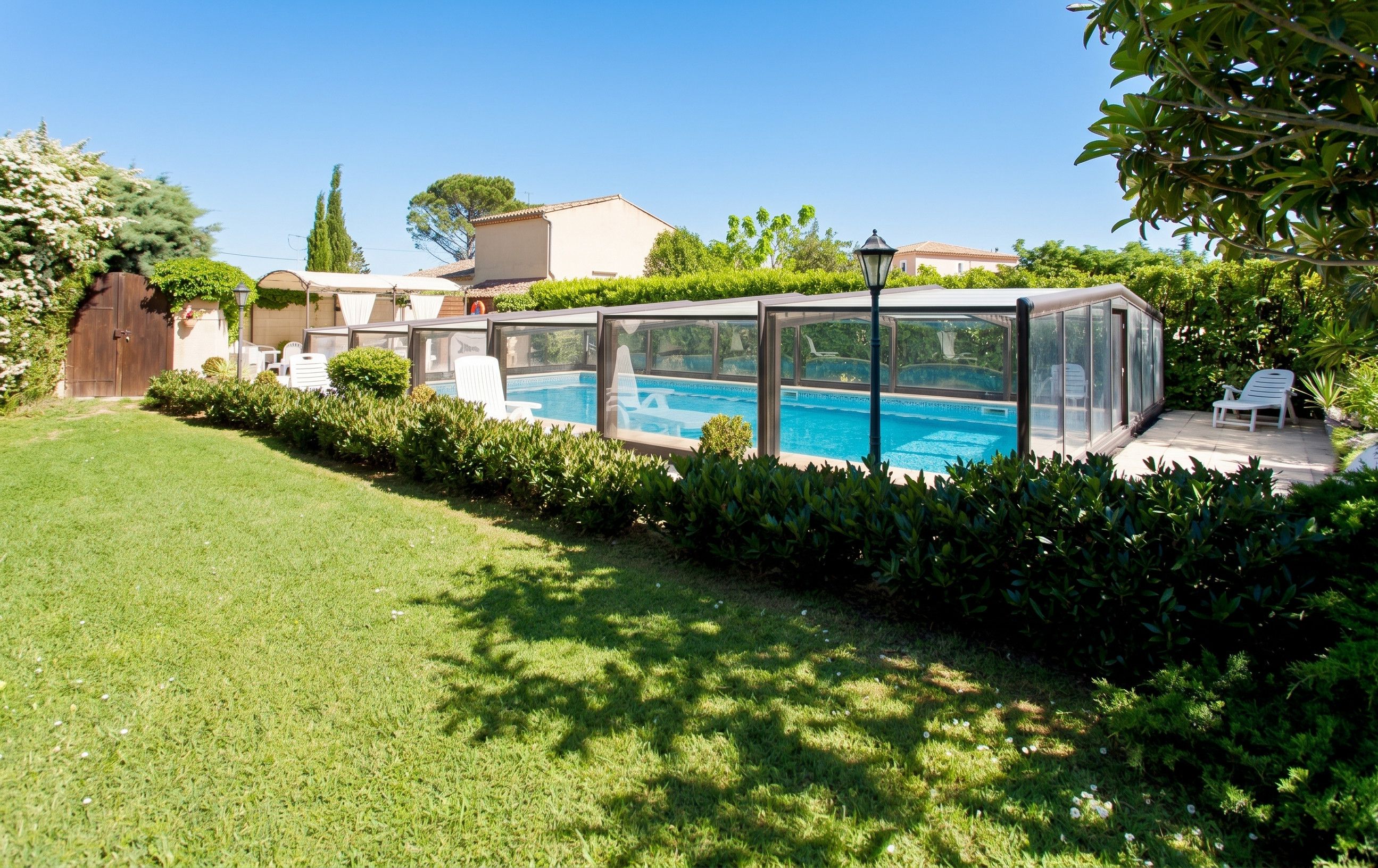 A backyard with a swimming pool, a covered patio area, and a wooden fence.