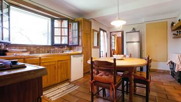 A kitchen with wooden cabinets, a dishwasher, a dining table with chairs, and a hanging light fixture.