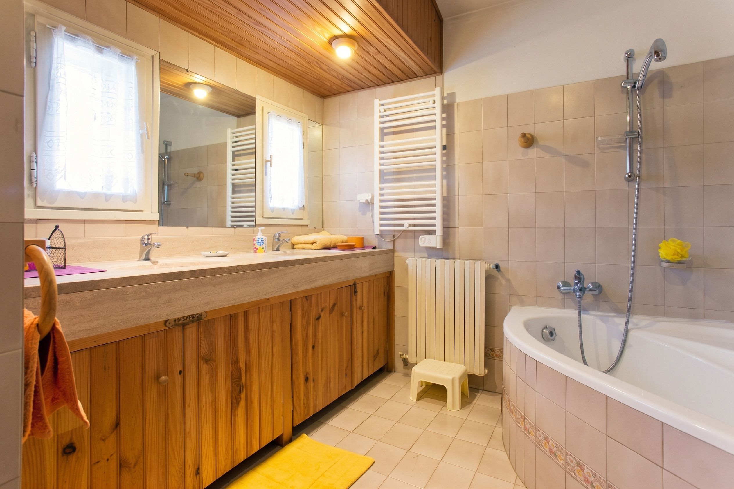 A bathroom with wooden cabinets, a bathtub, a shower, and a small stool.