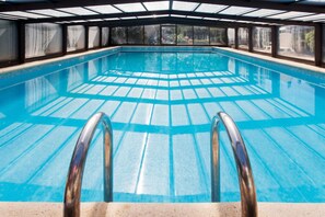 An indoor swimming pool with clear blue water, a tiled floor, and a metal ladder leading into the pool. - Homerez - Provencal Villa with Pool in Barbentane (Barbentane)
