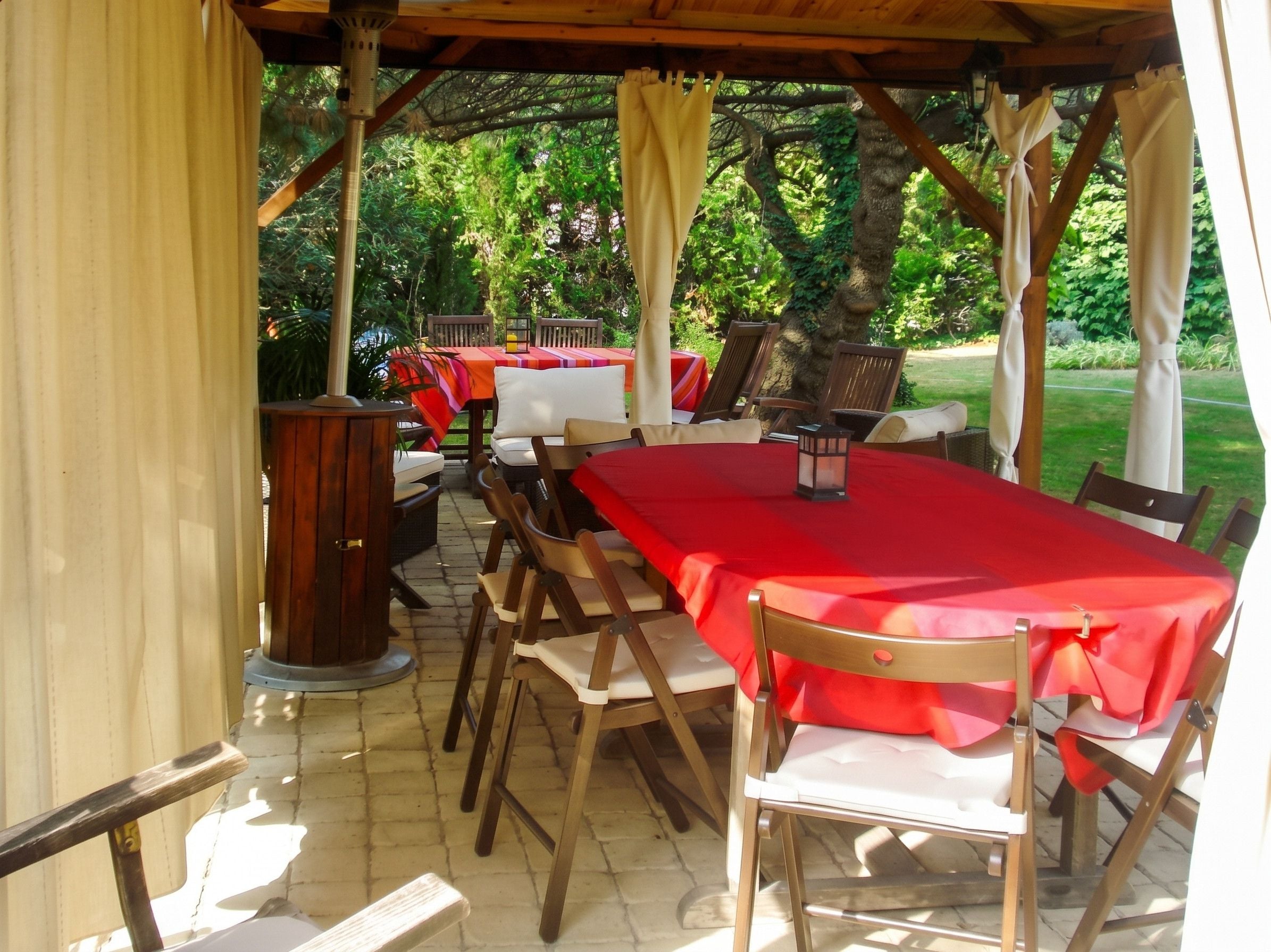 Un espacio comedor al aire libre con techo, mesas y sillas de madera, un armario de madera y un farol.