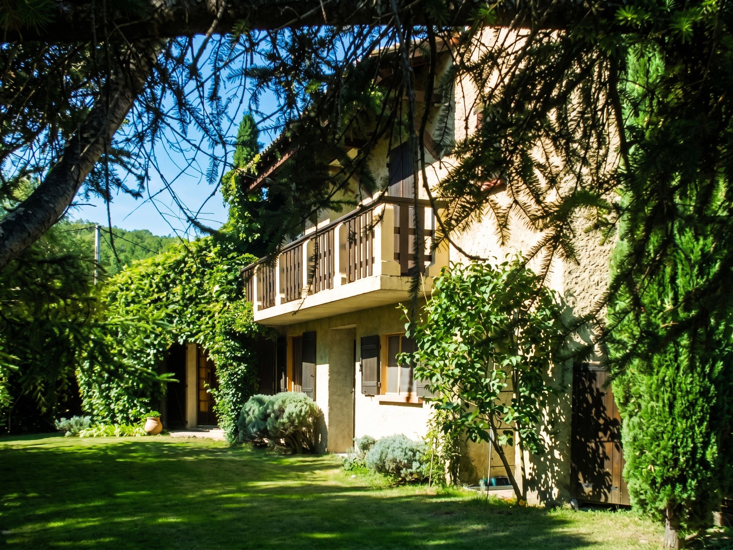 A two-story building with a balcony, surrounded by lush greenery and trees.