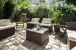 Een terras buiten met rieten meubels, waaronder banken en stoelen, op een geplaveid oppervlak.