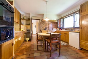 A kitchen with wooden cabinets, a dining table with chairs, a built-in oven, and a window. - Homerez - Provencal Villa with Pool in Barbentane (Barbentane)