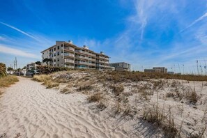 Un hotel a più piani con un sentiero sabbioso che vi conduce, circondato da dune.