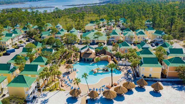 Un complejo turístico con varias edificaciones, una piscina central y una zona de playa con tumbonas y sombrillas.