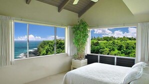 A bedroom with a bed, a ceiling fan, a window with a view of the ocean, and a potted plant. - Pali Ke Kua 226  Coastal, Ocean & Mountain Views! (Princeville)