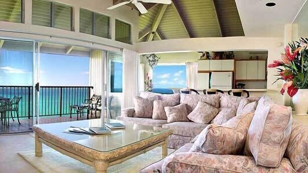 A spacious living area with a large sofa, a coffee table, and a balcony with a view of the ocean. - Pali Ke Kua 226  Coastal, Ocean & Mountain Views! (Princeville)