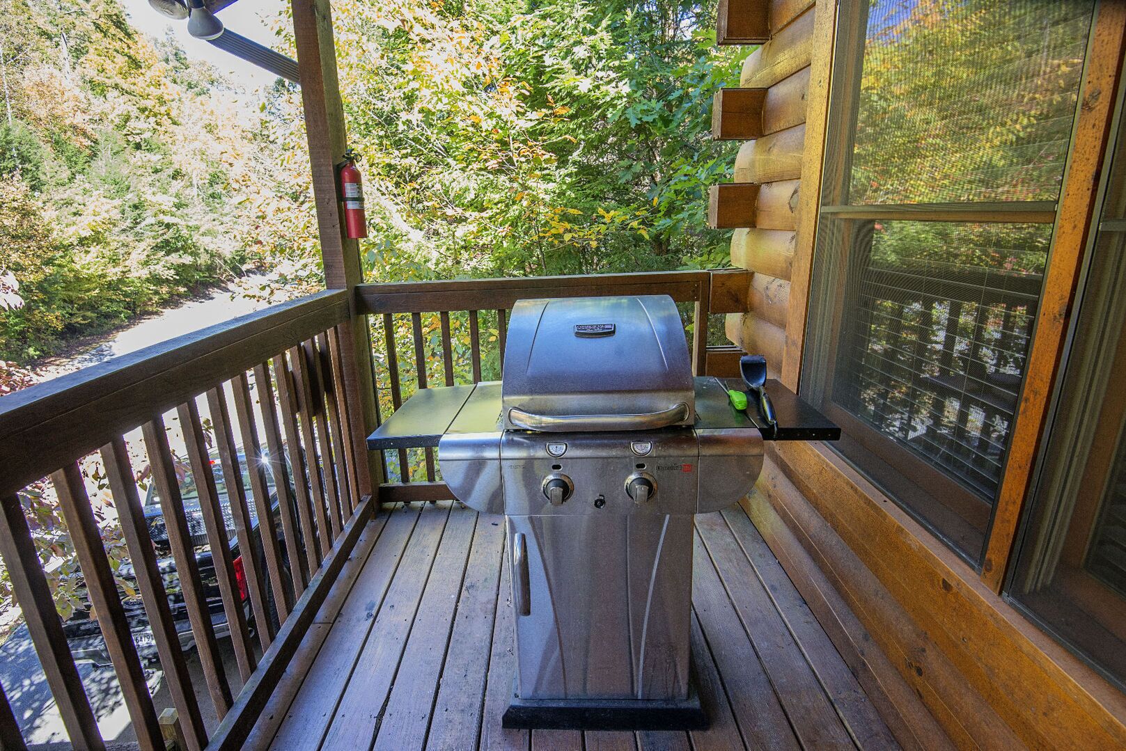 En balkong med en grill, en brandsläckare och utsikt över träd.
