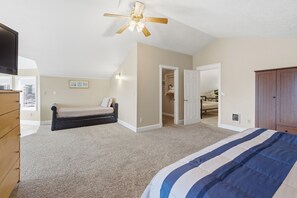 Een slaapkamer met een bed, een plafondventilator, een kast en een deur naar een andere kamer.