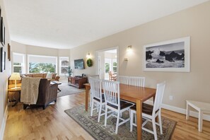 A spacious living area with a wooden dining table, white chairs, a sofa, and a fireplace.