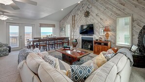 A spacious living room with a fireplace, a television, and a dining area with a view of the ocean.