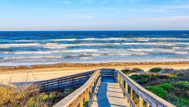 A wooden boardwalk leading to a beach with waves crashing onto the shore.