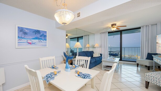 Een ruime woonkamer met een eettafel voor vier personen, een blauwe bank en een balkon met uitzicht.