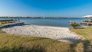 Een strand met een houten bankje, een kleine palmboom en een prieel met stoelen.