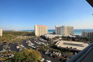 A high-rise hotel with multiple floors, a parking lot with various vehicles, and a clear view of the ocean. - Remodeled. Luau 6705 in Sandestin.Tram, wifi, larger Studio with balcony (Miramar Beach)