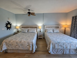 A hotel room with two beds, a ceiling fan, bedside lamps, and a sun-shaped wall decoration.