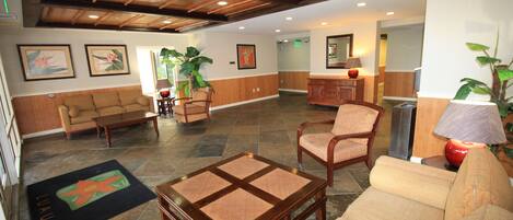 A spacious lobby with a high ceiling, a sofa, a coffee table, a dining table, and chairs. There are framed pictures on the walls and a potted plant.