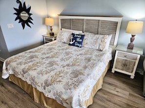 Un dormitorio con una cama grande, dos mesitas de noche, un espejo fijado a la pared y un adorno con forma de sol en la pared.