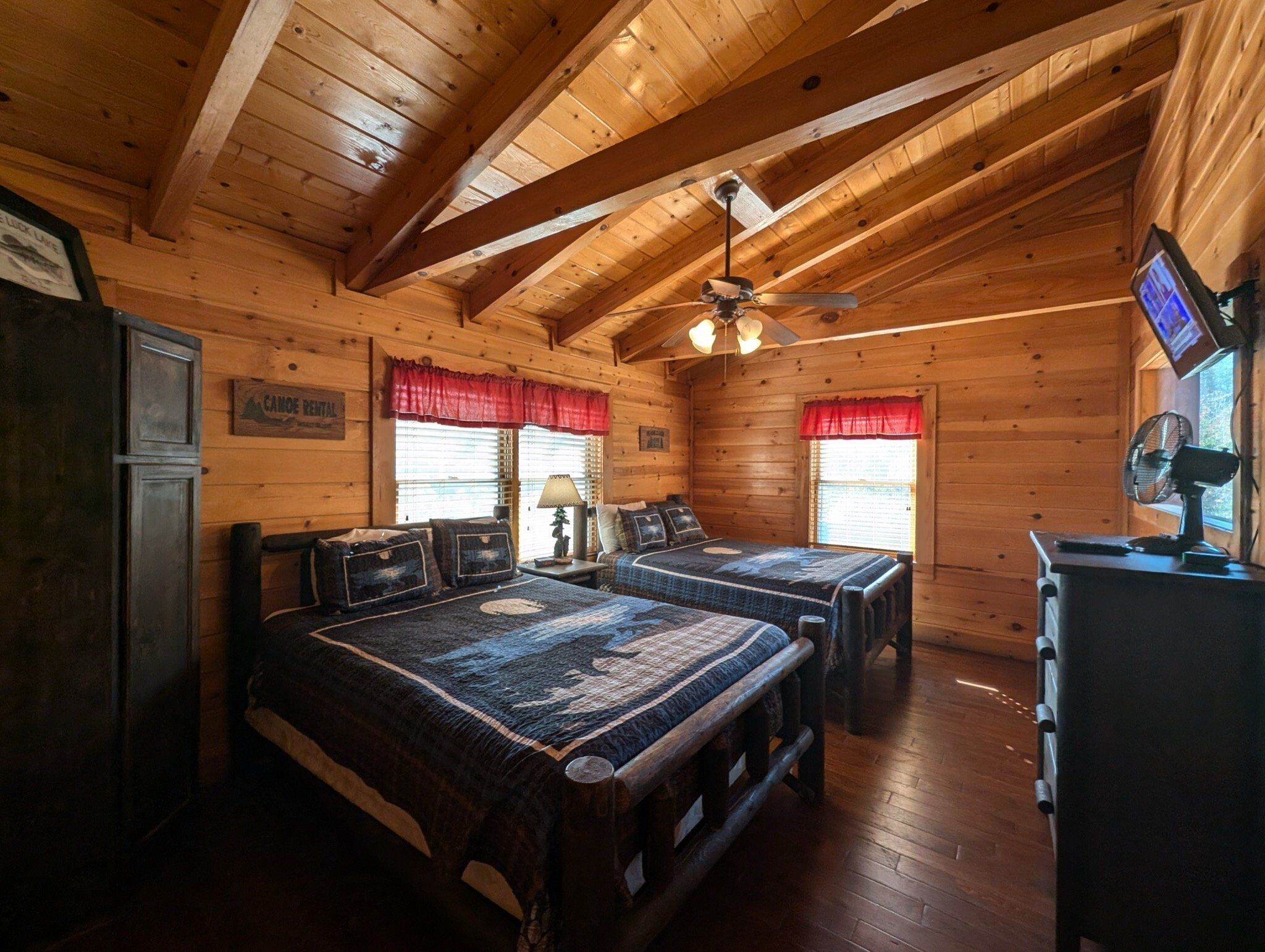 Une chambre de style cabane avec deux lits, un ventilateur de plafond et un téléviseur.