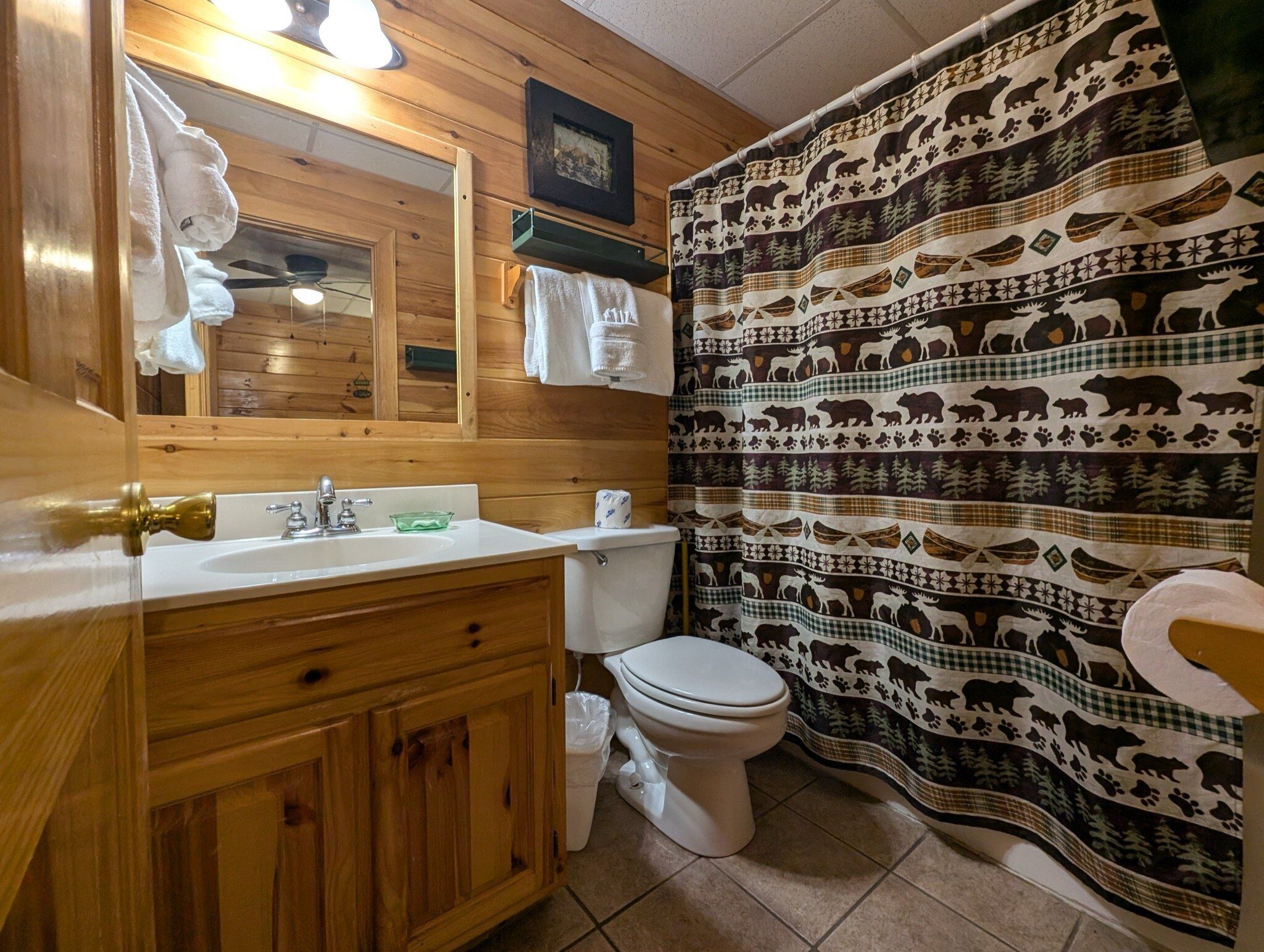 A bathroom with a wooden vanity, a sink, a toilet, and a shower curtain with animal patterns.