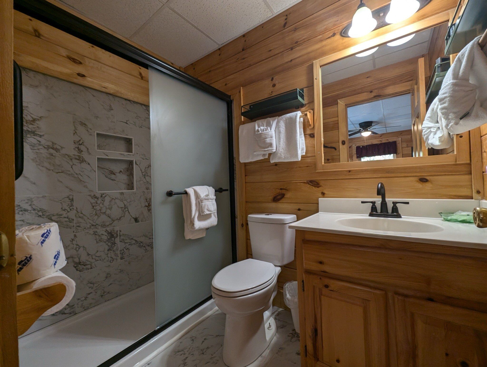 A bathroom with a wooden interior, a toilet, a sink, and a shower area.
