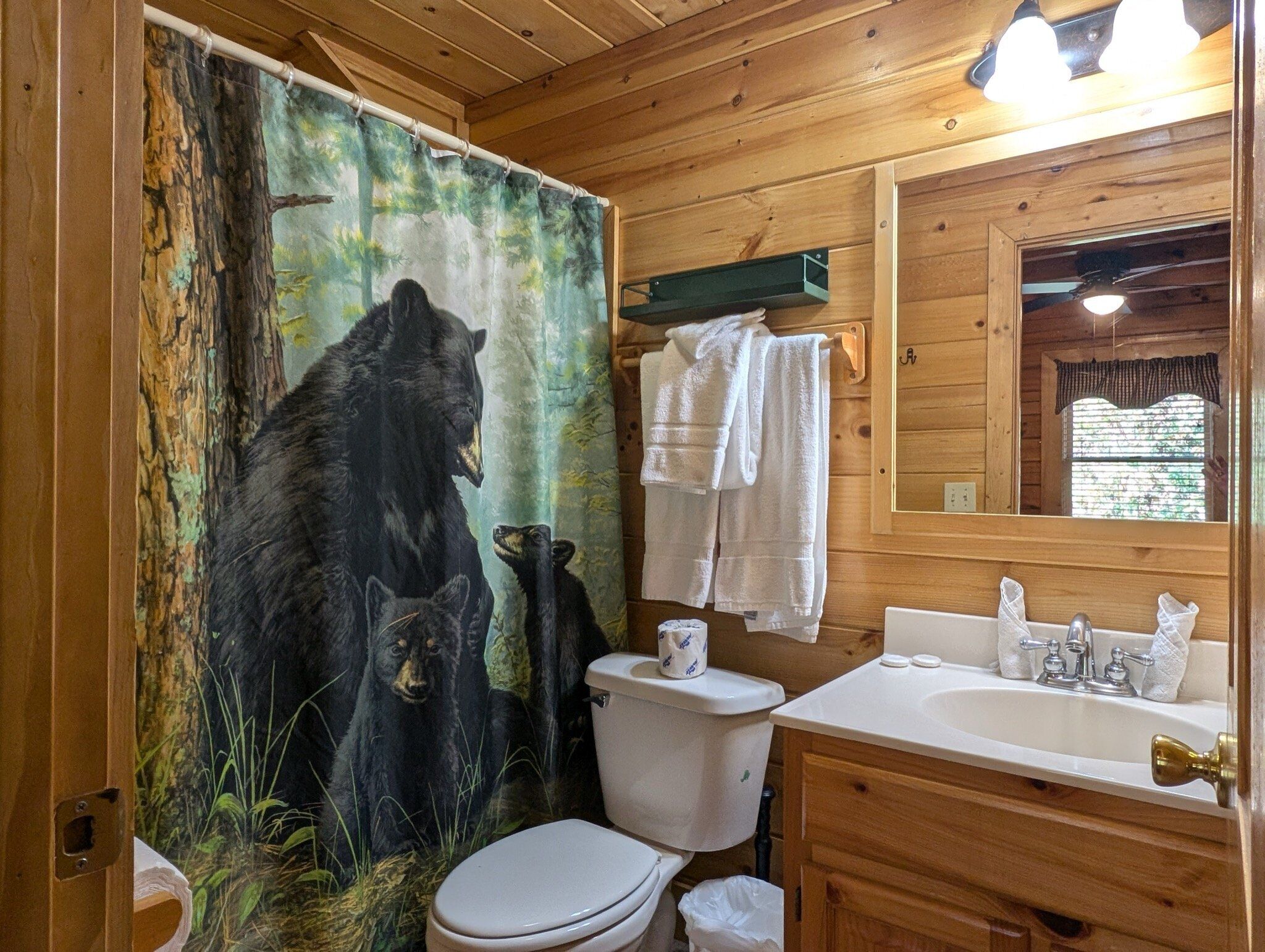 Une salle de bain avec une fresque représentant un ours, des murs en bois, des toilettes, un lavabo et un miroir.